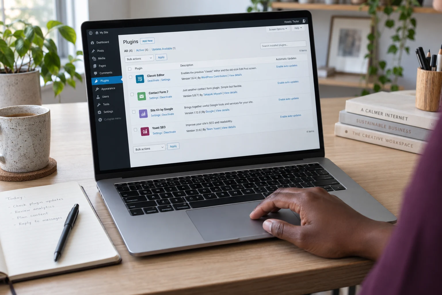 Close-up of a website plugin list on a laptop beside a notebook.